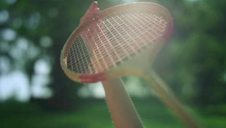 closeup hand holding wooden badminton racket in golden sunlight in park.