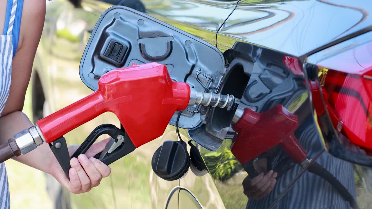 A person refuels a car with a red gas nozzle under bright daylight, highlighting energy and transportation