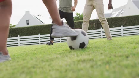 diverse male friends playing football in garden on sunny day