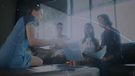 Female collaborator leaning forward handing document to team in lounge with business data overlay