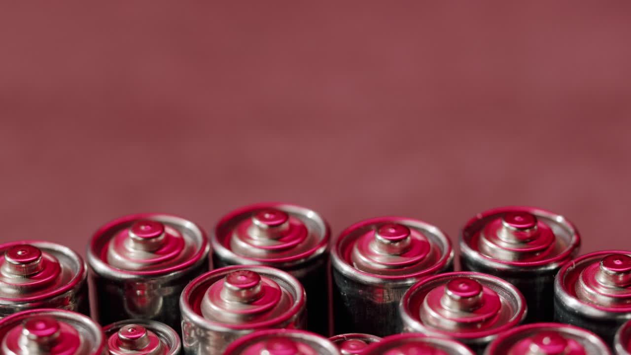 Silver batteries AA and AAA in neon light close-up. Double-A battery is a standard size single cell cylindrical dry battery. Batteries are common in portable electronic devices. An AA battery is composed of a single electrochemical cell that may be either a primary battery or a rechargeable battery.