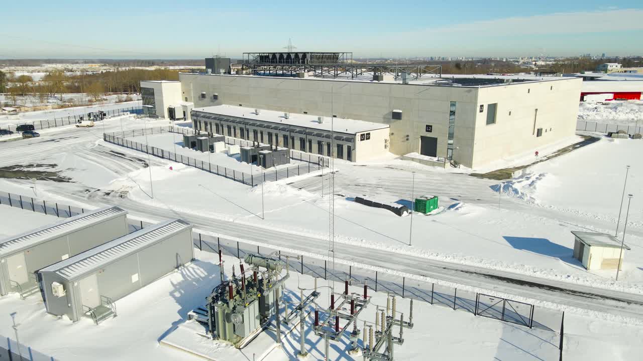 Ascending aerial reveal of secure AI data center with rooftop cooling systems and transformer yard operating in bright winter conditions
