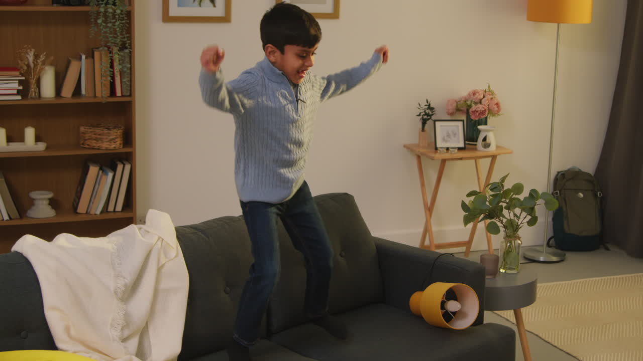 Disruptive Young Boy Behaving Badly At Home Jumping On Sofa And Throwing Cushions Around Lounge 4
