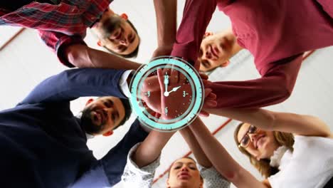 Animation-of-clock-over-work-colleagues-stacking-hands-in-background