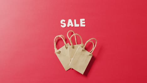 sale text in white with three gift bags on red background with copy space