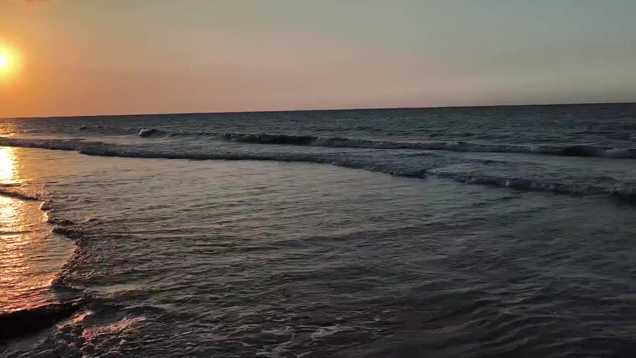 Dolci Onde dell'Oceano che si Infrangono su una Spiaggia Sabbiosa al Tramonto