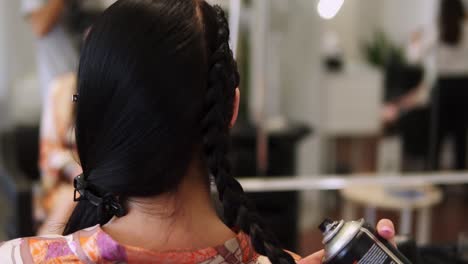 Female-stylist-applying-hairspray-fixing-plaiting-hairstyle-on-brunette-hair-back-view-slow-motion.-Hairdresser-finishing-hairdo-making-final-touch-with-spray.-Overview