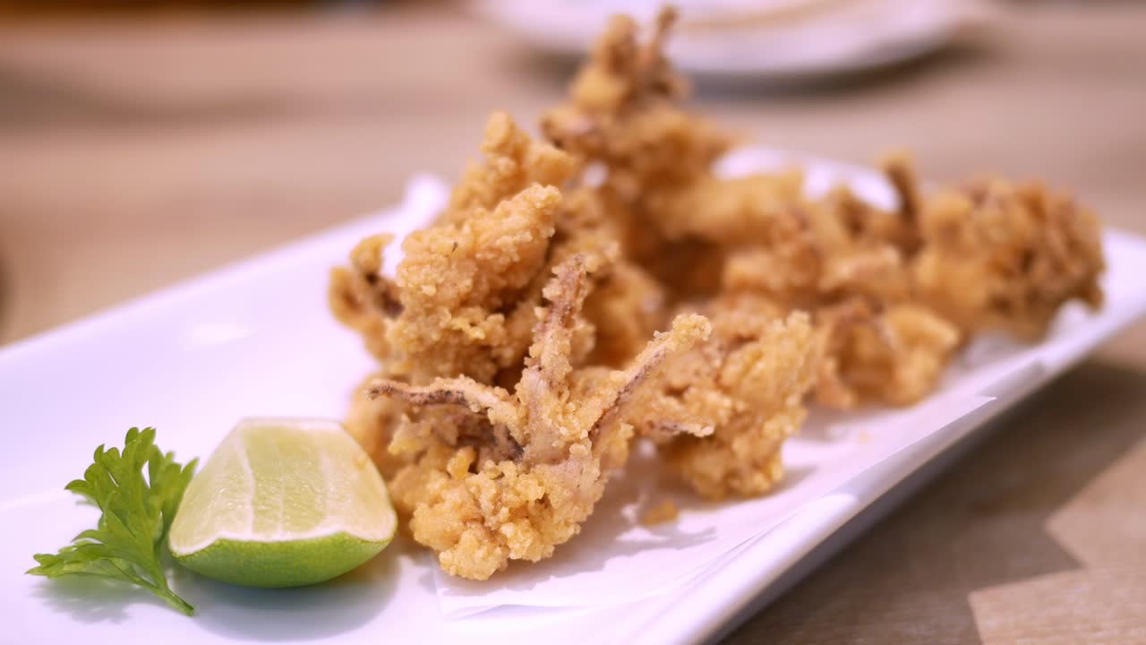 Un primo piano di frutti di mare fritti gustosi e croccanti su un piatto, serviti con lime e mangiati con un paio di bacchette.