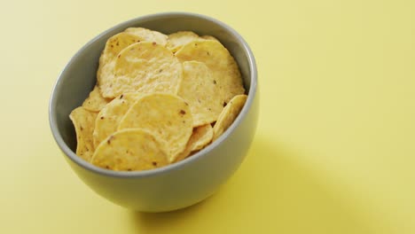 Close-up-of-chips-in-a-bowl-with-copy-space-on-yellow-surface