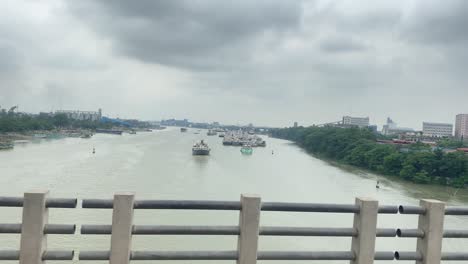 Driving-on-bridge-in-Sylhet-over-Surma-river-with-port-in-distance,-side-view