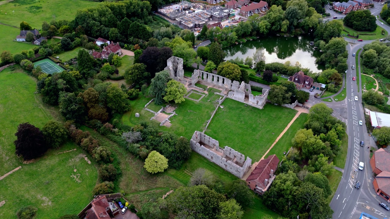 Wide-angle aerial drone pans left over Bishop’s Waltham Palace ruins, capturing the historic site surrounded by autumn trees and fields glowing warmly in the golden sunset light.