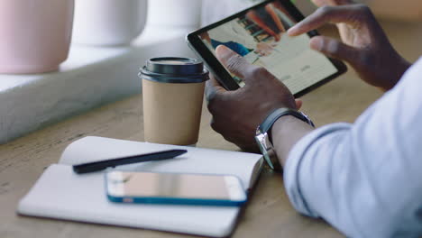 african american businessman using tablet computer in cafe browsing corporate documents enjoying drinking coffee reading email on mobile device screen browsing online close up hands