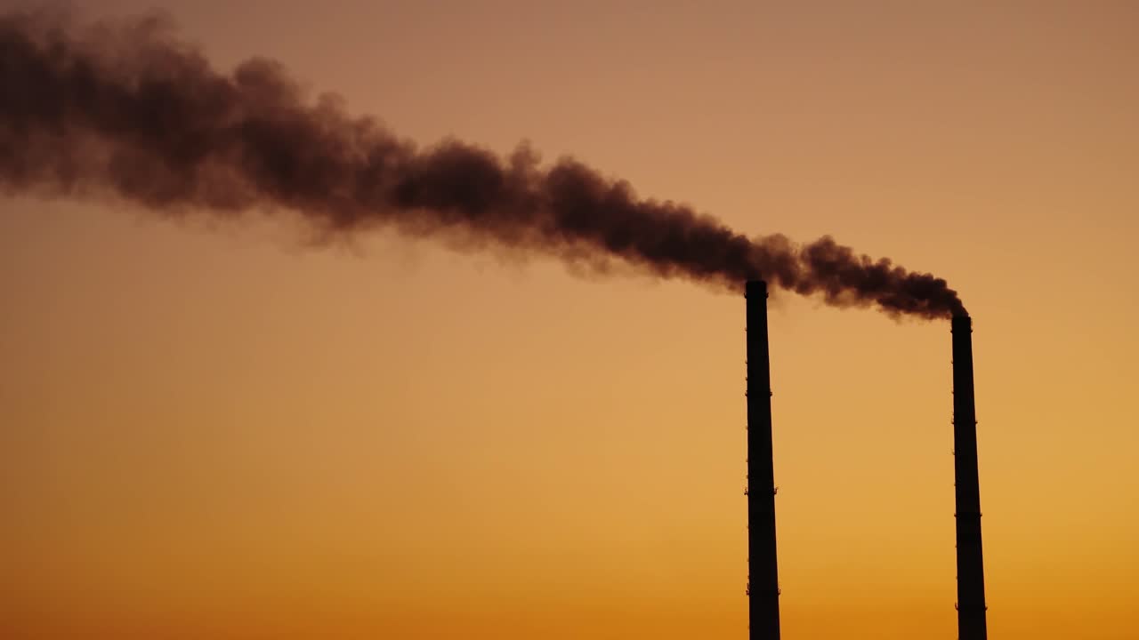 Dirty emissions on the orange sky background. Two pipes with dark smoke at sunset. Ecological disaster. Air pollution.