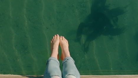 Vista-Superior-Mujer-Descalza-Piernas-Colgando-Sobre-El-Agua-Niña-Disfrutando-De-Las-Vacaciones-De-Verano-Sentada-En-El-Embarcadero-De-La-Playa