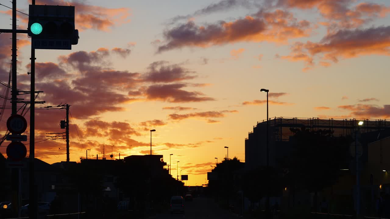 Dramatic sunset with orange and pink clouds silhouetting city buildings and a traffic light