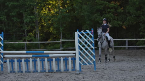 Young-woman-jumps-horse-over-an-obstacle-during-her-training-in-an-arena.-Young-woman-jumps-horse-over-an-obstacle-during-an-event-in-an-arena.-Sport.-Aims