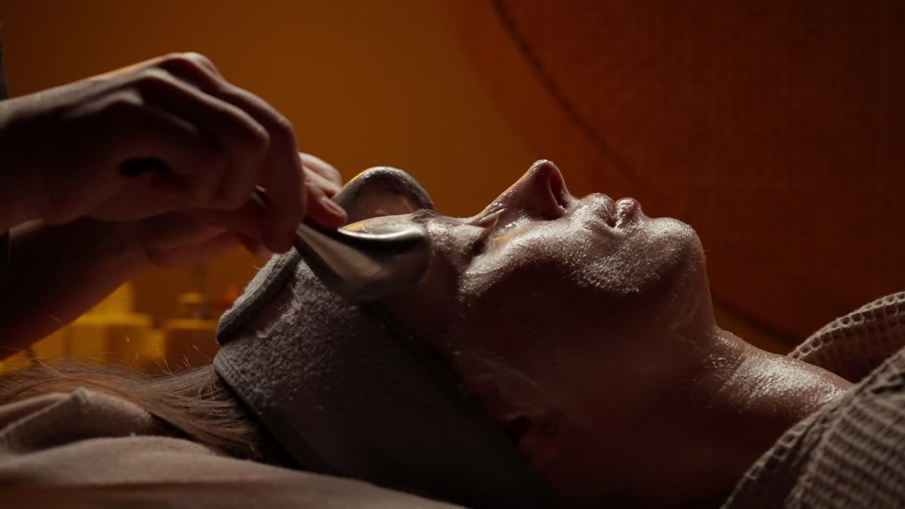 Kvinde modtager afslappende ansigtsmassage med kolde kugler på spa