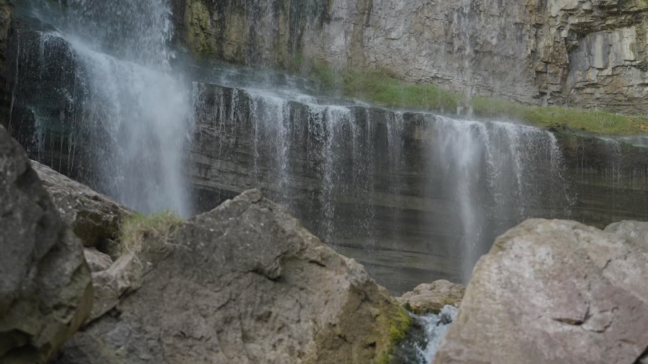 Water cascades over a rocky ledge surrounded by boulders in a peaceful natural setting