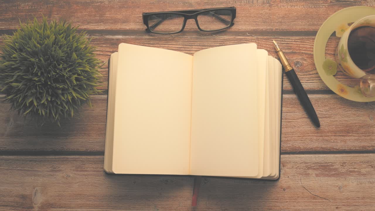 Open Notebook, Glasses, Pen, and Tea Cup on Wooden Desk