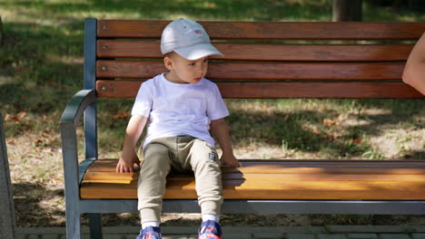 calm peaceful two-year-old toddler sitting still on the bench. cute baby boy resting in the park in summer.