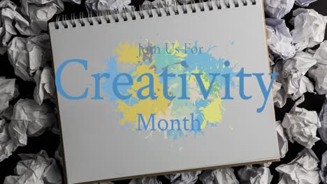 creativity month text over colorful paint stain against diary and multiple paper balls