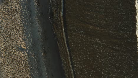 Vertical-shot-of-the-beach-with-small-waves-colliding-at-sunset