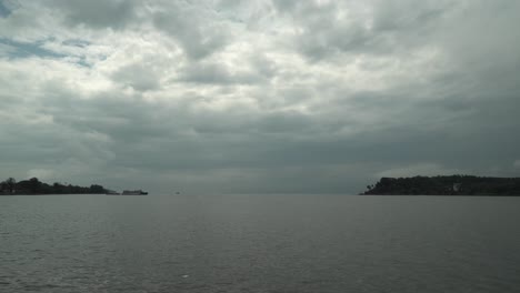 Toma-Amplia-De-Lapso-De-Tiempo-De-Un-Lago-Con-Aguas-Tranquilas-Con-Botes-Flotantes-Y-Una-Vista-De-Las-Islas-Con-Bosques-Y-El-Cielo-Nublado