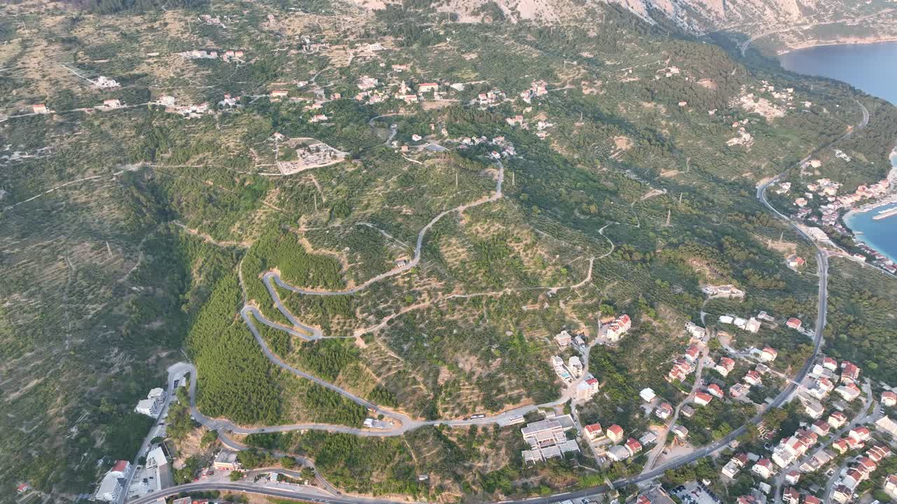 Podgora’s turquoise beach and promenade transition to majestic Biokovo peaks as sun sets, aerial tilt