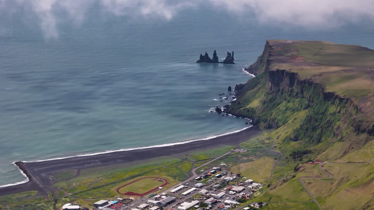 Aerial wide shot of basalt sea stacks at beach of Reynisdrangar near Vik, Iceland. Flight between clouds showing dramatic scene.