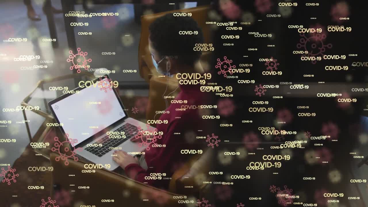 Animation of covid 19 text and icons over woman using laptop in office wearing face mask