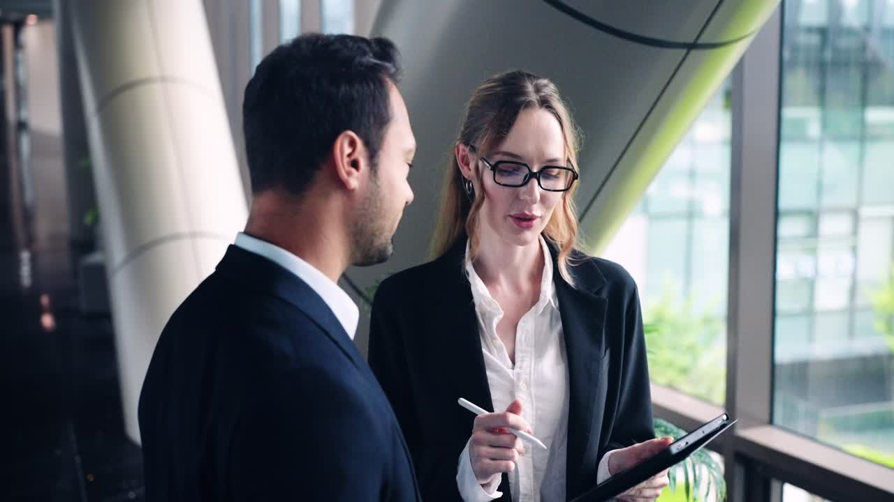 Happy male and female executives talk and smile while discussing business strategy and future plans near sunlit window in modern office