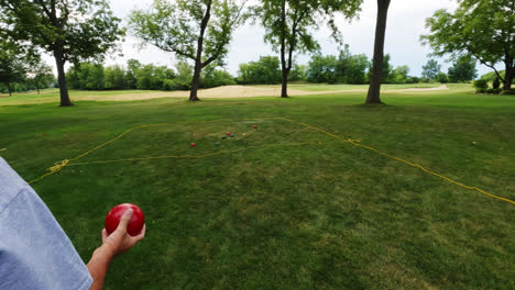 Shot-of-a-senior-caucasian-male-playing-traditional-boules-game-throwing-heavy-shiny-red-metal-ball-on-target-on-a-cloudy-day