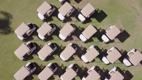 twisting aerial shot of several rows of parked golf carts on green grass