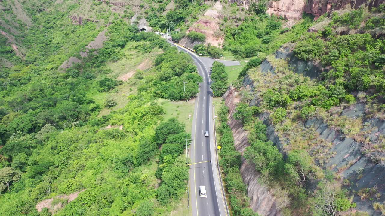 toma aerea, siguiendo un auto por un camino hasta llegar a terowogan en colombia con maravillosos colores verde y el gris del camino, es un camino dentro del pegunungan