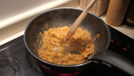 cooking and stirring vegan indian curry with wooden spoon in a pan