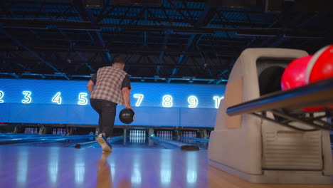 the camera follows one man throwing a bowling ball on the playing track and jumps rejoicing in the downed pins. one man bowling in slow motion