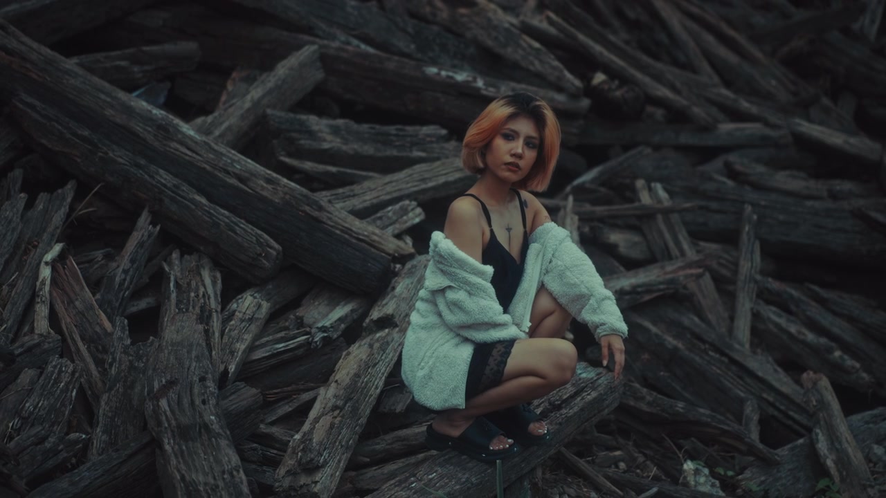 Young Woman with Short Hair Squatting Among Wooden Logs