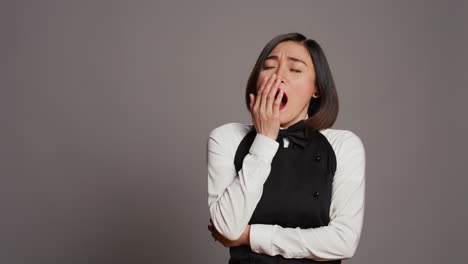 Exhausted-waitress-with-apron-yawning-over-grey-background