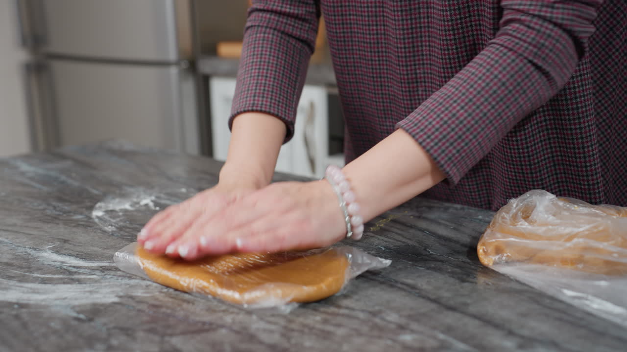 dama dando forma a la masa dentro de una bolsa de cuero blanco en el mostrador de la cocina mientras recoge la segunda masa para envolver, preparando productos horneados caseros en la cocina moderna con iluminación cálida, encimera de polvo de harina