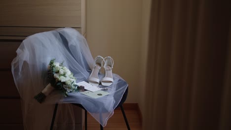 wedding shoes, bouquet, and invitation placed on a chair with a soft veil