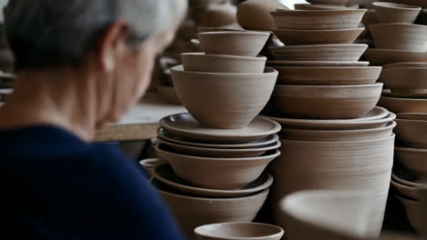 artisan surrounded by stacks of handmade pottery in a studio