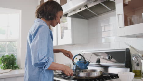 Millennial-African-American-woman-standing-in-the-kitchen-cooking-on-the-hob,-waist-up,-side-view