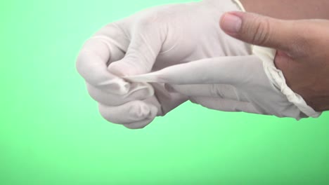 a close-up shot of a woman's hands taking off white latex gloves and hanging them together on a green screen background