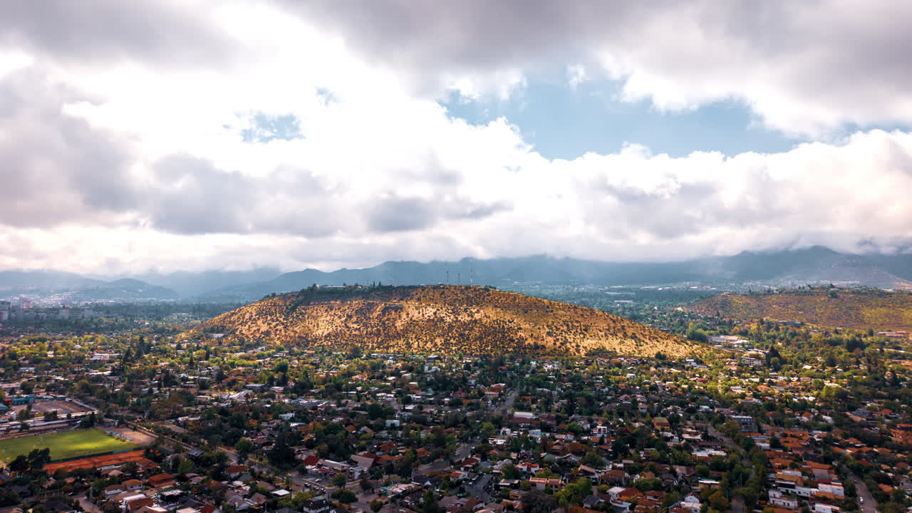 Aerial hyperlapse zooming in over Cerro San Cristóbal in Santiago de Chile, with dramatic skies and city views in the background