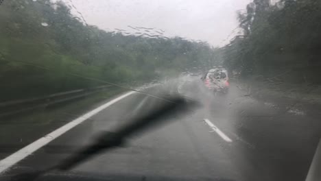 vista del parabrisas desde un interior conduciendo en una fuerte lluvia con limpiadores encendidos y vehículos de adelantamiento