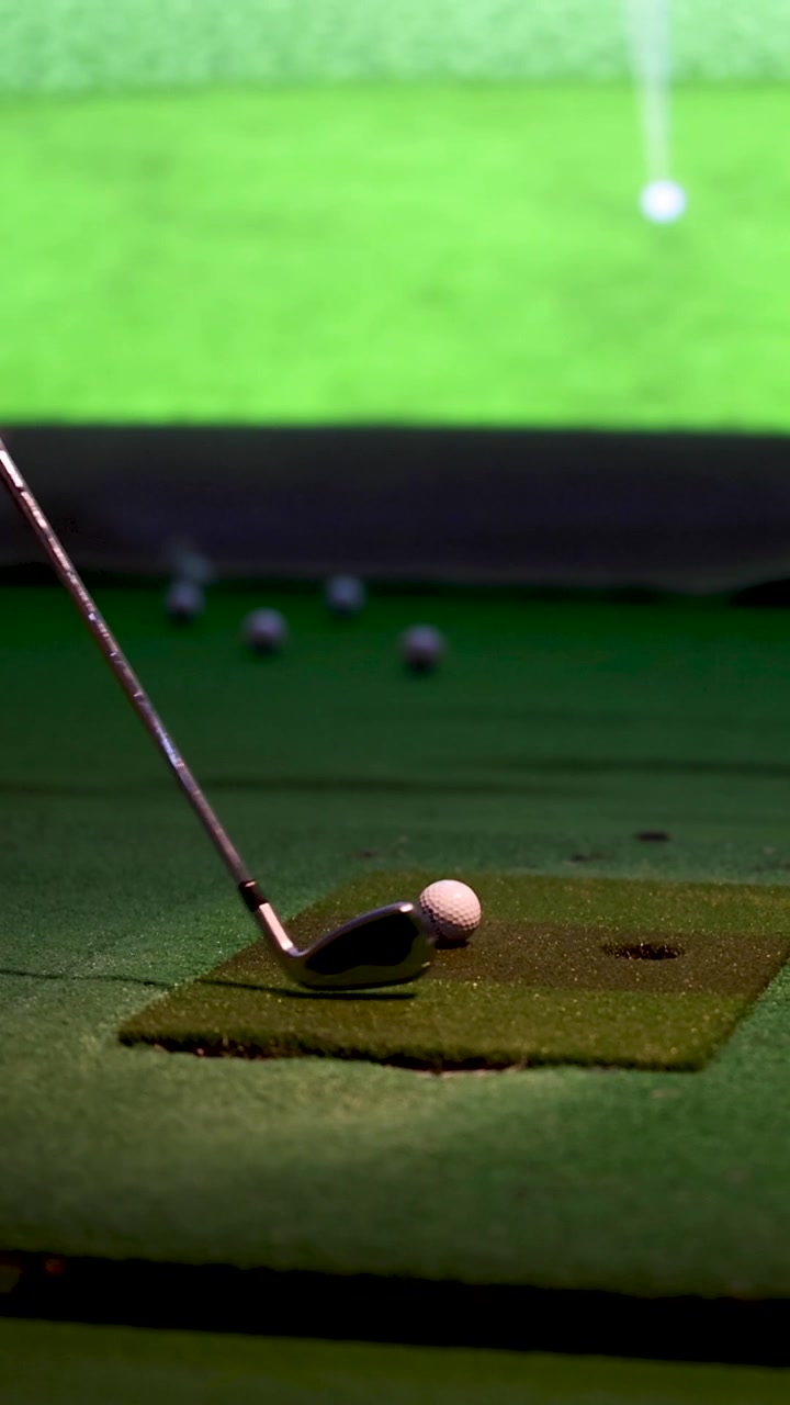 Una ripresa verticale dettagliata di una mazza da golf che colpisce una palla in un campo pratica al coperto