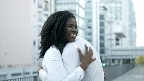 mujer afroamericana sonriente abrazándose con un amigo en la calle