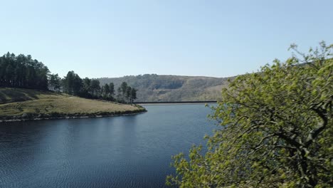 aerial shot panning right in close proximity to a tree revealing kinder reservoir dam wall