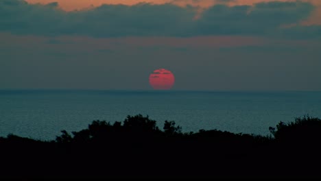 astonishing red sun setting below sea horizon, cumulus grey clouds, static