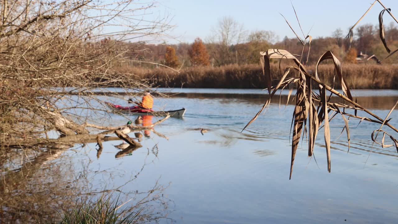 Man on a canoe rowing on a lake in autumn, warm relaxed ambience